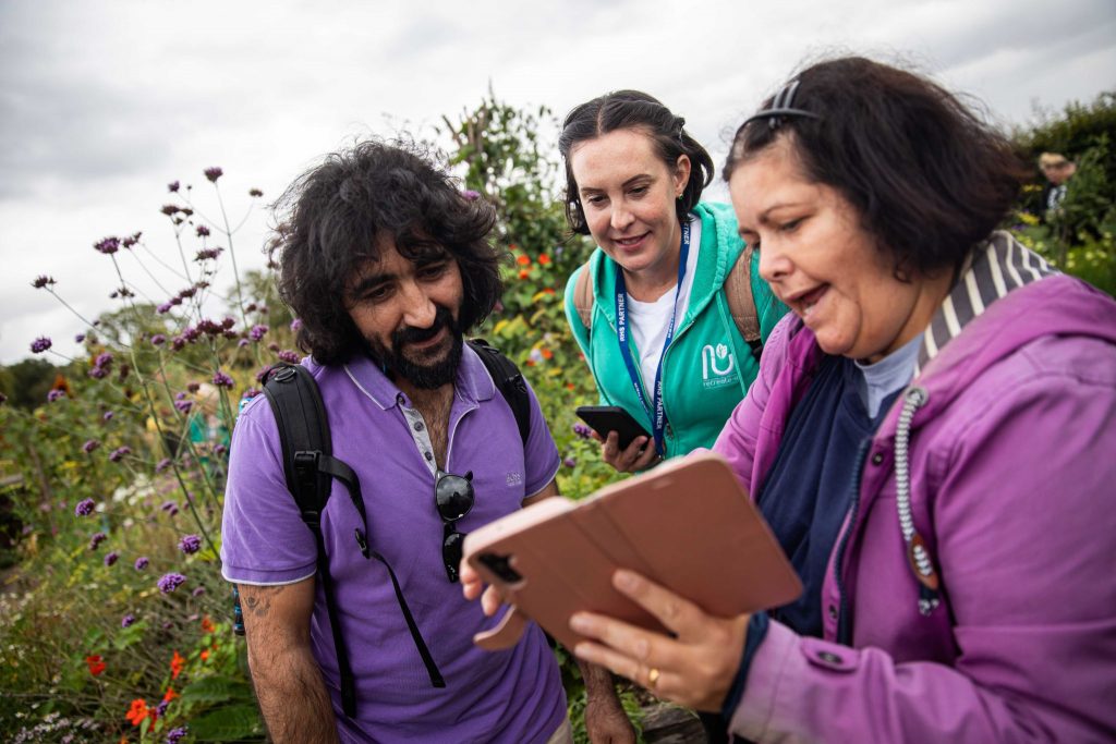 Anoosh Ariamehr working with two community members, surrounded by plants and flowers.